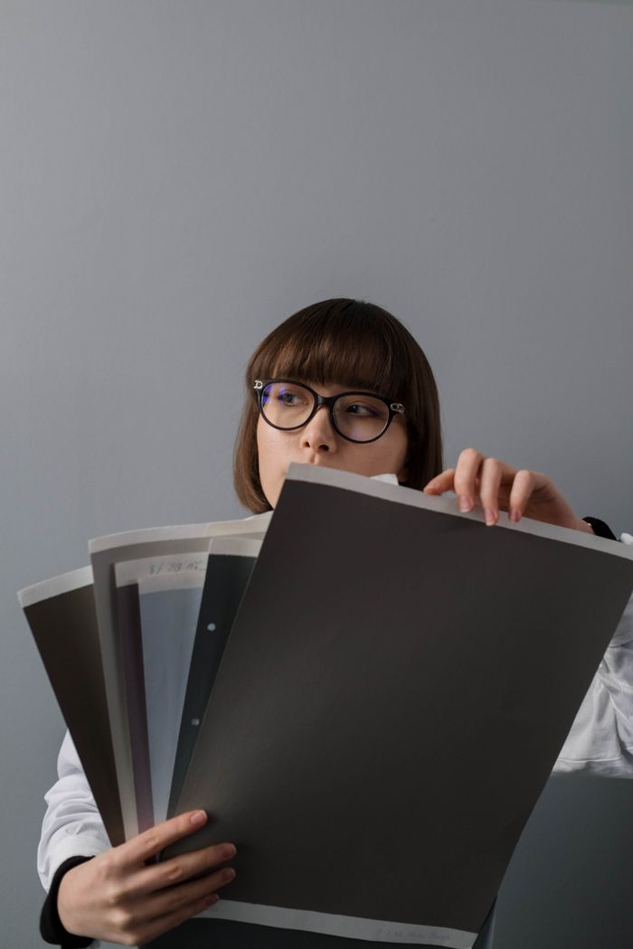 A woman wearing glasses examines various paper samples, offering a minimalistic and modern aesthetic.